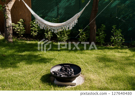 Relaxing Backyard Oasis with White Hammock and Fire Pit. Cozy Outdoor Living Space, Lush Greenery, Warm Lighting, Peaceful Summer Scene Relaxing Backyard Oasis with White Hammock and Fire Pit. Cozy Outdoor Living Space, Lush Greenery, Warm Lighting, Peaceful Summer Scene 127640480