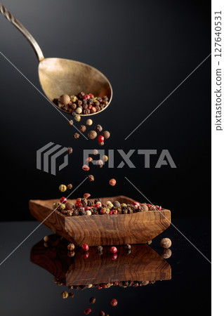 Black, red, white, and allspice peppercorns is poured in wooden dish. 127640531