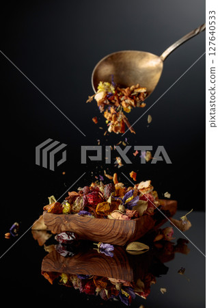 Various dried herbs and spices is poured into a wooden dish. 127640533