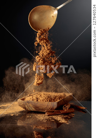 Cinnamon powder is poured into a wooden dish. 127640534