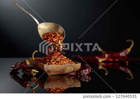 Dry red chili peppers and crushed chili flakes on a black reflective background. 127640535