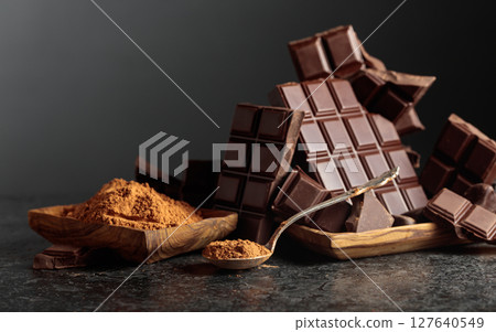 Broken dark chocolate bar and cocoa powder on a black background. 127640549