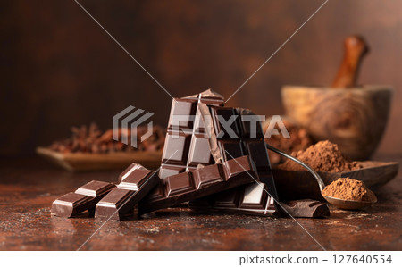 Broken dark chocolate bar and cocoa powder on a brown table. 127640554
