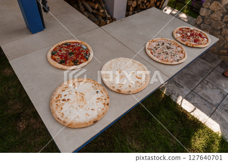 Variety of Delicious Artisan Pizzas on Concrete Table Outdoors with Green Grass, Sunlit View, Rustic Wooden Details, Food Photography Variety of Delicious Artisan Pizzas on Concrete Table Outdoors with Green Grass, Sunlit View, Rustic Wooden Details, Food Photography 127640701