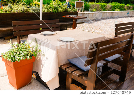 Outdoor restaurant table set for two. Summer dining, natural ambiance, and casual elegance in a sunny garden setting. Outdoor restaurant table set for two. Summer dining, natural ambiance, and casual elegance in a sunny garden setting. 127640749