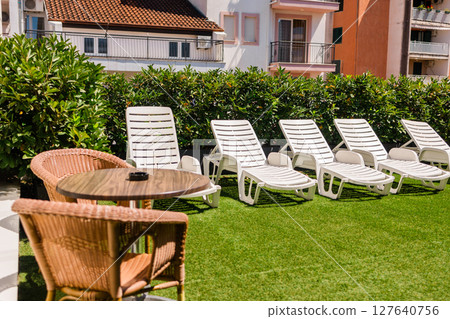 Rooftop lounge area with sunbeds and wicker chairs. Outdoor relaxation, summer leisure, and casual urban hospitality in a sunny hotel courtyard. 127640756