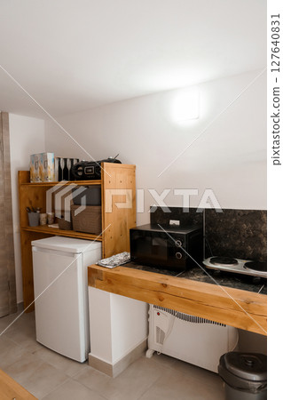 Minimalist Kitchenette Setup in White Room with Wooden Countertop and Small Appliances, Modern Interior Design, Refrigerator, Microwave, and Compact Space 127640831