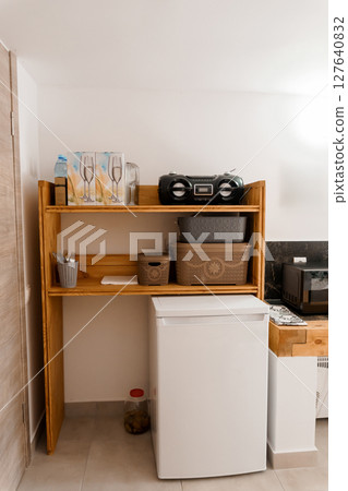 Cozy Kitchenette Interior with Wooden Shelves, White Appliances, Woven Baskets, and Essential Utensils, Natural Light, Rustic Style, Beige Tones. Cozy Kitchenette Interior with Wooden Shelves, White Appliances, Woven Baskets, and Essential Utensils, Natural Light, Rustic Style, Beige Tones. 127640832