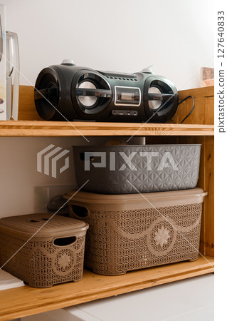 Organized Laundry Room Shelf with Black Boombox, Wicker Baskets, and Beige Storage Containers on Wooden Structure, White Walls. 127640833