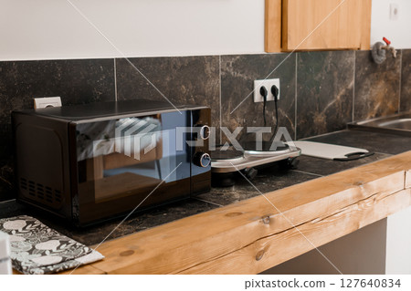 Modern Black Microwave Oven on Wood Countertop Against Dark Tile Backsplash in Contemporary Kitchen Interior, Appliances and Home Decor 127640834