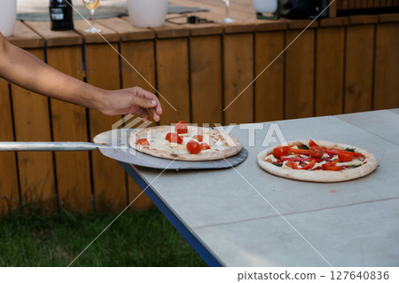 Backyard Pizza Party: Hand Placing Tomato Slices on Fresh Dough, Outdoor Wooden Bar, Summer Evening, Natural Light, Rustic Style Backyard Pizza Party: Hand Placing Tomato Slices on Fresh Dough, Outdoor Wooden Bar, Summer Evening, Natural Light, Rustic Style 127640836
