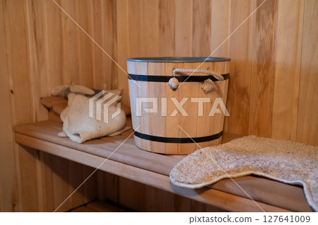 Wooden sauna interior with bucket, mittens, and towel on wooden shelf 127641009