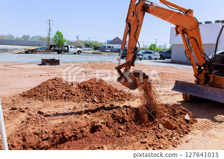 Heavy machinery digs into earth, moving red soil at construction site during works area. Heavy machinery digs into earth, moving red soil at construction site during works area. 127641013