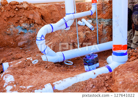 Workers install sewage PVC pipes in trench at construction site, ensuring proper drainage plumbing setup. Workers install sewage PVC pipes in trench at construction site, ensuring proper drainage plumbing setup. 127641022