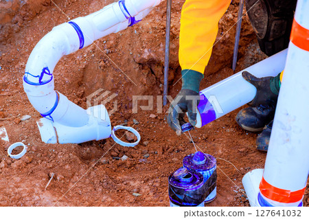 Worker connects new plumbing sewage pipes while fixing drainage system in residential yard during work day 127641032