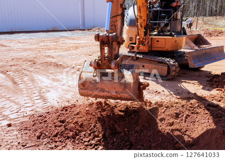Construction worker operates an excavator to dig reshape ground in works construction area 127641033