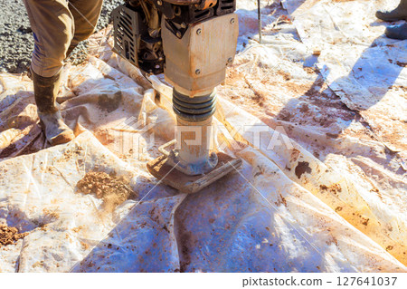 Construction worker uses tamper to compact soil on job site in preparate to foundation slab 127641037