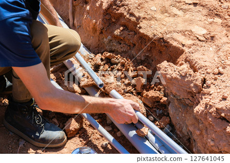 Worker is fixing electrical pipes in trench with dirt rocks scattered around in works day Worker is fixing electrical pipes in trench with dirt rocks scattered around in works day 127641045