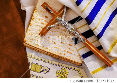 Crucifix on tallit prayer shawl traditional matzah religious symbols are arranged on table for Passover celebration. 127641047