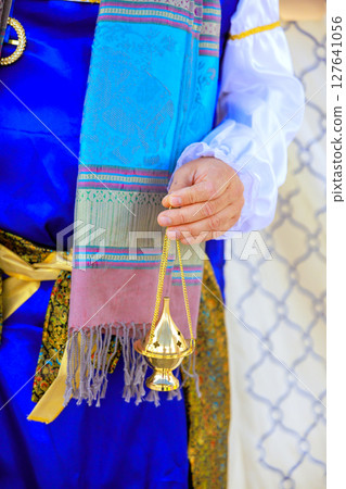 Jewish high priest in vibrant traditional attire holds brass incense burner in festive during Jew holy cultural event. 127641056