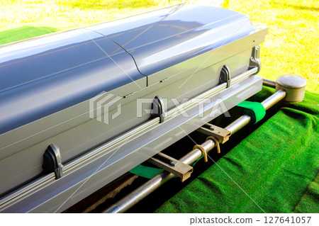 Casket placed on green surface, prepared for burial while surrounded by serene cemetery atmosphere 127641057