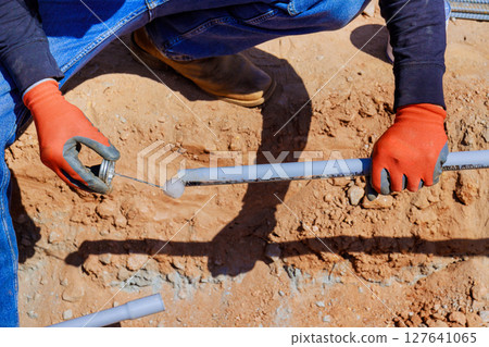 Electrician laborer wearing gloves works diligently to connect two electrical pipe sections on construction site Electrician laborer wearing gloves works diligently to connect two electrical pipe sections on construction site 127641065