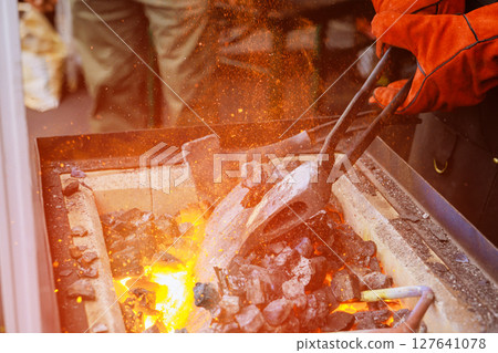 Metal is being shaped in blacksmith shop as sparks fly from glowing coals, during axe making skilled craftsmanship. 127641078