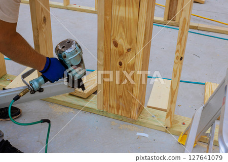 Carpenter secures wooden planks with air nail gun, focusing on precision at construction site Carpenter secures wooden planks with air nail gun, focusing on precision at construction site 127641079