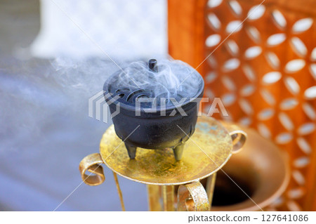 Fragrant smoke swirls from decorative incense burner at an outdoor gathering, enhancing peaceful atmosphere. 127641086
