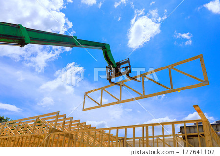 Forklift telehandler crane lifts large wooden truss into place, helping to construct new home under works day Forklift telehandler crane lifts large wooden truss into place, helping to construct new home under works day 127641102