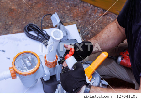 Contractor works diligently on pool pump, adjusting components at well lit outdoor works 127641103