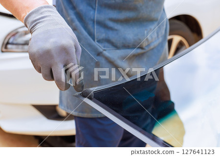 Skilled technician worker carefully applies adhesive to windshield in an auto service shop during replacements windshield Skilled technician worker carefully applies adhesive to windshield in an auto service shop during replacements windshield 127641123