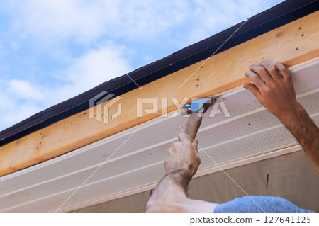 Carpenter hands hammering roof siding trim while working on home improvement during works day 127641125