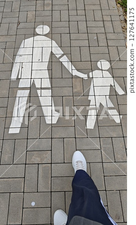 Pedestrian path marking of an adult and child holding hands on tiled pavement. Concept of safety, walkability and family-friendly urban infrastructure Pedestrian path marking of an adult and child holding hands on tiled pavement. Concept of safety, walkability and family-friendly urban infrastructure 127641175