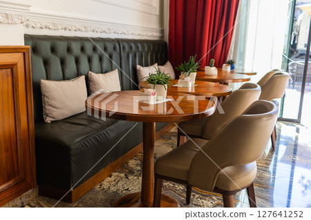 Stylish seating area in modern cafe interior. Elegant furniture, natural light, and greenery create a calm, welcoming environment for relaxation or conversation. Stylish seating area in modern cafe interior. Elegant furniture, natural light, and greenery create a calm, welcoming environment for relaxation or conversation. 127641252