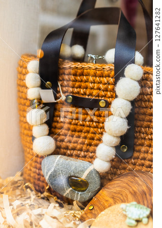 Handcrafted wool necklace with stone pendant on wicker bag. Natural materials, rustic fashion, and boho accessory design in artisan boutique display. Handcrafted wool necklace with stone pendant on wicker bag. Natural materials, rustic fashion, and boho accessory design in artisan boutique display. 127641282