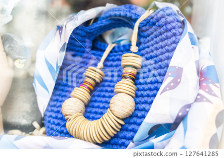 Colorful wooden necklace displayed on blue knitted bag. Handmade fashion, summer accessories, and artisan style in boutique showcase. 127641285