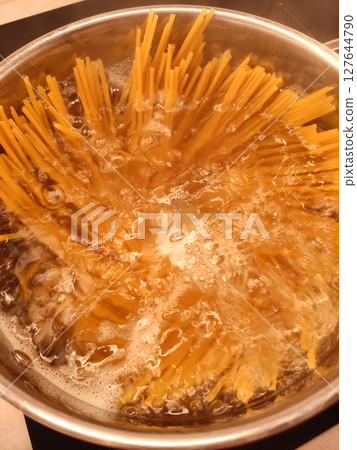Long spaghetti being cooked in boiling water in metal pot Long spaghetti being cooked in boiling water in metal pot 127644790