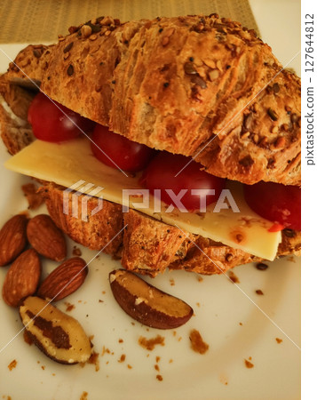 Whole grain croissant filled with cheese and tomatoes accompanied by almonds and brazil nuts 127644812
