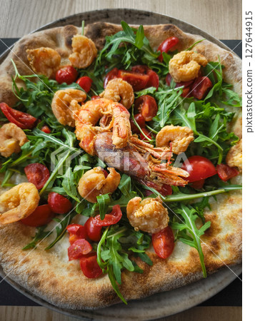 Crispy pizza topping featuring fresh arugula, succulent shrimp, vibrant cherry tomatoes on rustic italian style crust in aosta region 127644915