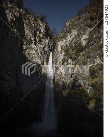 Powerful waterfall cascading down rugged cliffs in aosta, italy, surrounded by natural rock formations and bathed in soft november light Isollaz waterfall Powerful waterfall cascading down rugged cliffs in aosta, italy, surrounded by natural rock formations and bathed in soft november light Isollaz waterfall 127644922
