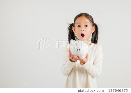 Asian little kid girl holding piggy bank and looking at camera at studio isolated on white background, Happy kindergarten child lifestyle smiling with is white piggybank, Thai personal money savings 127646275