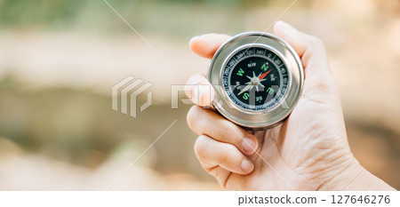 In forest a hiker relies on a compass to navigate through the confusion. compass in the traveler hand signifies leadership and exploration she maps her position and embarks on journey of discovery. 127646276