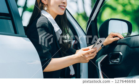 A woman/businesswoman getting out of a car with a smartphone 127646698