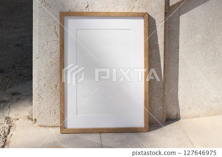 Vertical wooden picture frame leaning against stone wall in sunlight. Textured beige tiles background. Summer outdoor natural, minimal backdrop. Empty poster mockup, branding display. Vertical wooden picture frame leaning against stone wall in sunlight. Textured beige tiles background. Summer outdoor natural, minimal backdrop. Empty poster mockup, branding display. 127646975