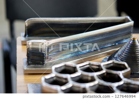 Objects printed on 3D printer from filament of molten metal on table. Object printed by 3D printer from metal. Additive manufacturing solution. Object created on 3D printer from melting metal thread 127646994