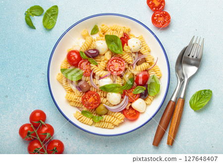 Italian pasta salad with fusilli, cherry tomatoes, mozzarella, olives, basil on blue background top view, Italian cuisine 127648407