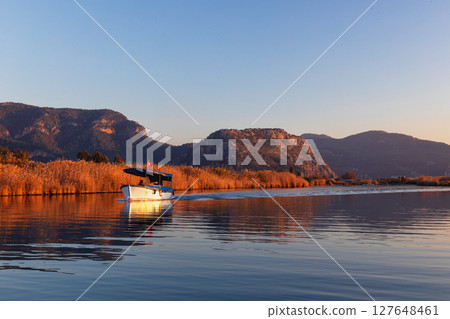 Touristic boat trip on sunset by Dalyan River from ancient Greek city Kaunos in Caria to Iztuzu or Turtle beach. Popular place for family travel on summer vacation. Dalyan, Mugla, Turkey Touristic boat trip on sunset by Dalyan River from ancient Greek city Kaunos in Caria to Iztuzu or Turtle beach. Popular place for family travel on summer vacation. Dalyan, Mugla, Turkey 127648461