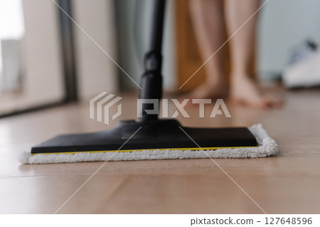 Cropped shot of unrecognizable man washing hardwood floor with steam cleaner mop in modern apartment, ensuring hygiene and cleanliness, close-up. Concept of modern housekeeping appliance. 127648596