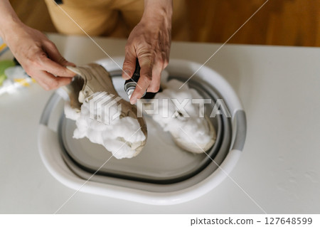 Cleaning white sneakers with foam spray, male hands washing athletic shoes in bathroom sink, focusing on footwear hygiene and thorough maintenance, closeup. Concept of maintaining hygiene, cleanliness 127648599